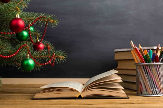 Open book on a desk with pencils next to a Christmas tree