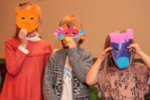 Young students holding crafted paper masks over their faces