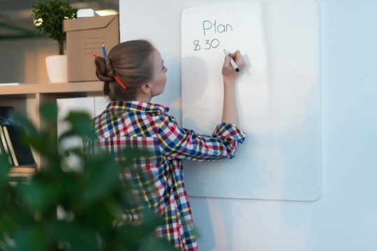 Young woman standing and writing plans on a whiteboard.