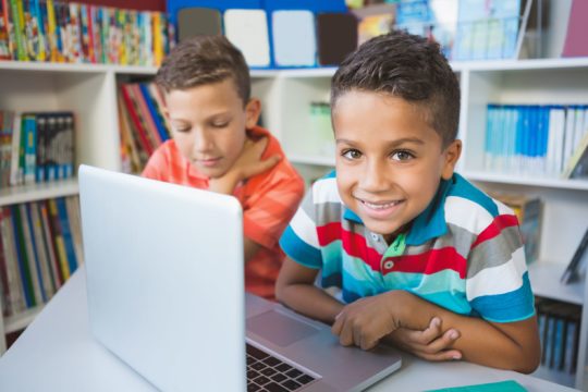 Two young boys sitting together and using a laptop.