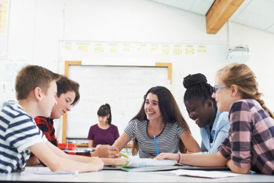 Group of smiling students working together at a table in a classroom.