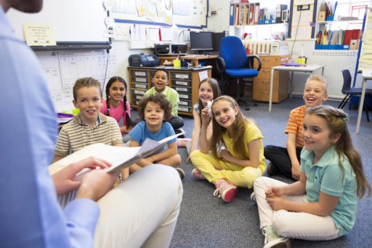 Group of students listening to a teacher read them a story.