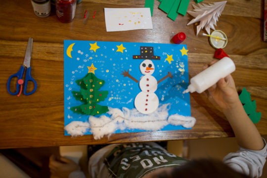 Young child sitting at a table creating a winter scene with art supplies.