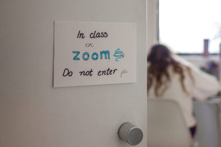 A students working at a desk with a sign on the door saying “in class on Zoom. Do not enter”