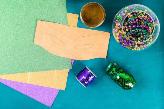 Craft supplies to make a Mardi Gras mask laid out on a table.