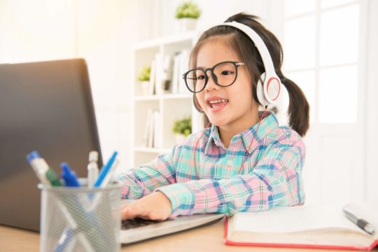 Young girl smiling and wearing headphones while using a laptop.