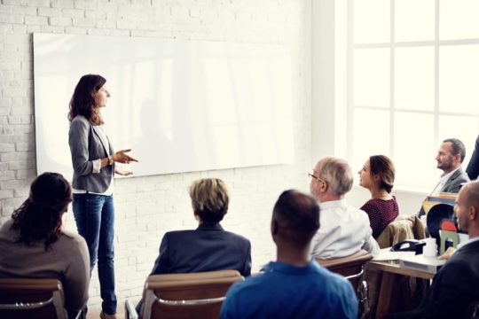 Woman in front of whiteboard talking to group of people