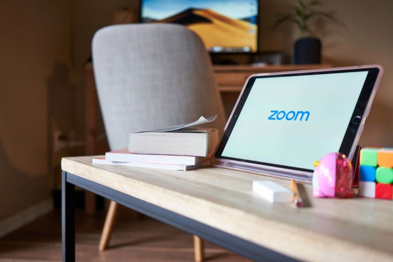 Tablet displaying ‘Zoom’ sitting on a coffee table with books and a pencil.