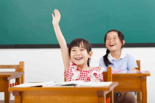 Smiling young girl in class with hand raised