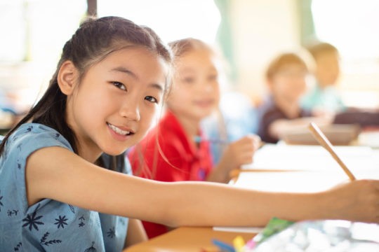 Young smiling girl writing at her desk in class