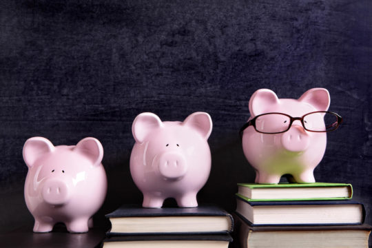 Three piggy banks on top of ascending stacks of books.