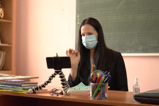 Teacher sitting at her desk recording a video on her phone.