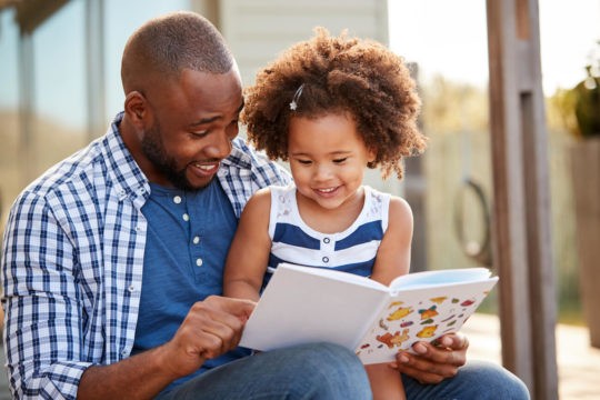 A dad and young daughter reading together.