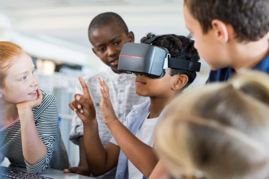 Group of young students standing together while one wears a virtual reality headset.