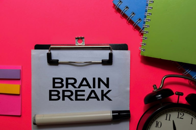 ‘Brain Break’ written on a clipboard surrounded by notebooks and a clock.