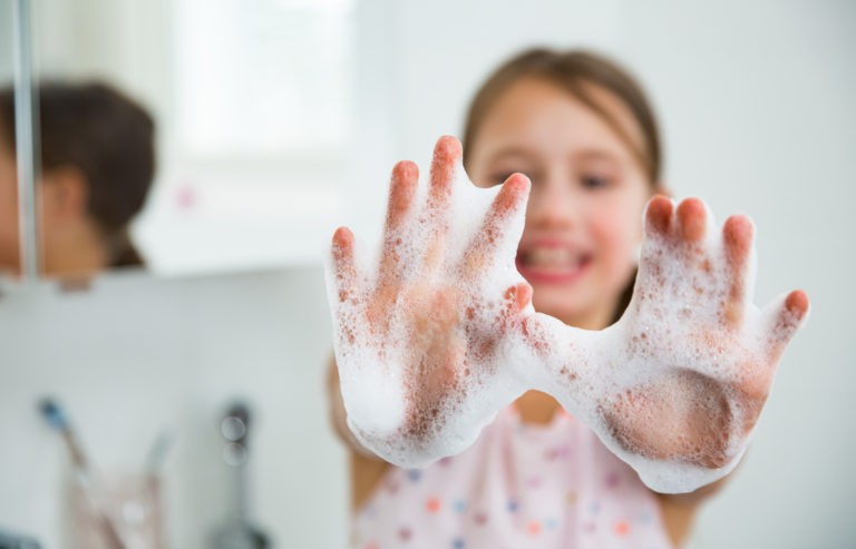Young girl holding up her soapy hands while washing them and smiling.
