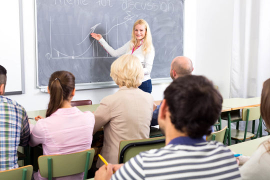 Teacher standing at the front of a classroom and leading a discussion with other teachers.