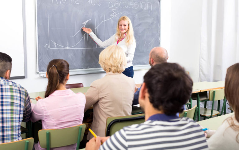 Teacher standing at the front of a classroom and leading a discussion with other teachers.
