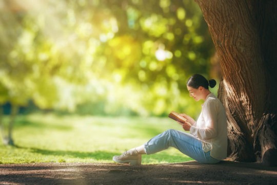 A woman sitting outside while reading a book.