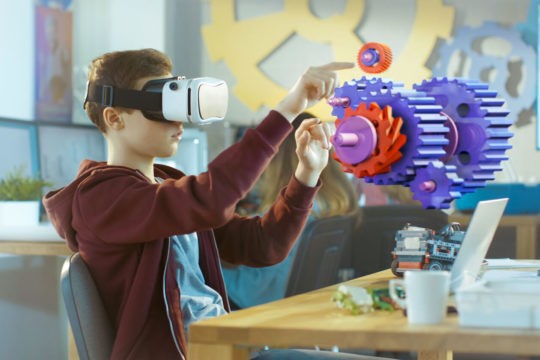 A boy wearing a virtual reality headset works in an interactive 3D environment.