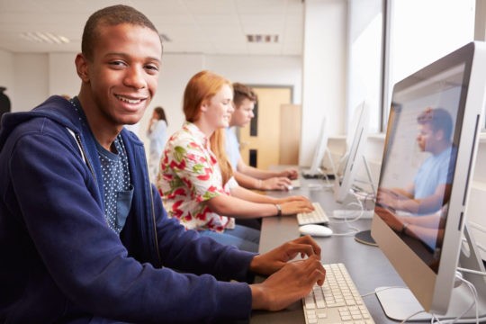 High school boy smiling while using a computer.