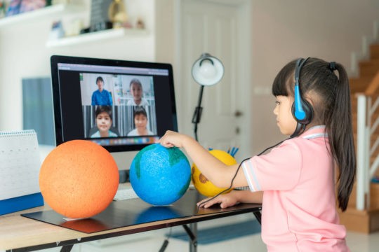 Young girl showing off a science project to her classmates over Zoom.
