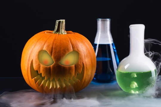 A scary jack-o-lantern sitting beside two beakers filled with colorful solutions.