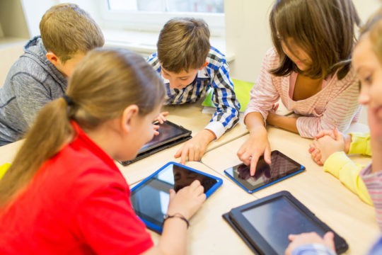 Group of young students using tablets at a shared table.