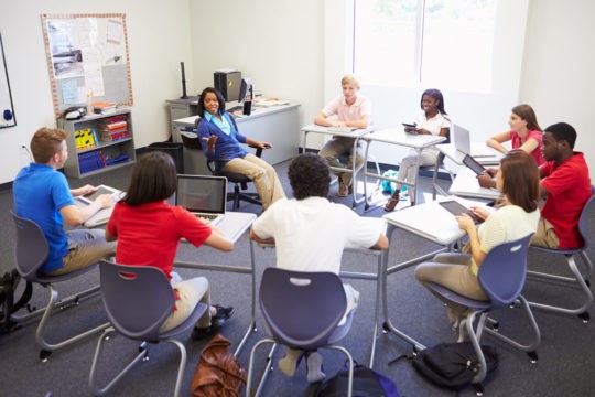 High school students sit in a circle, taking part in a classroom group discussion.