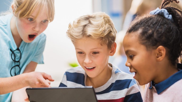 Two girls and boy excitedly use digital tablet computer in the classroom.
