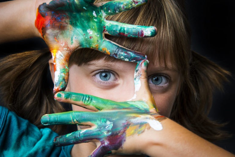 Young girl with hands covered in paint making a square for her to look through.