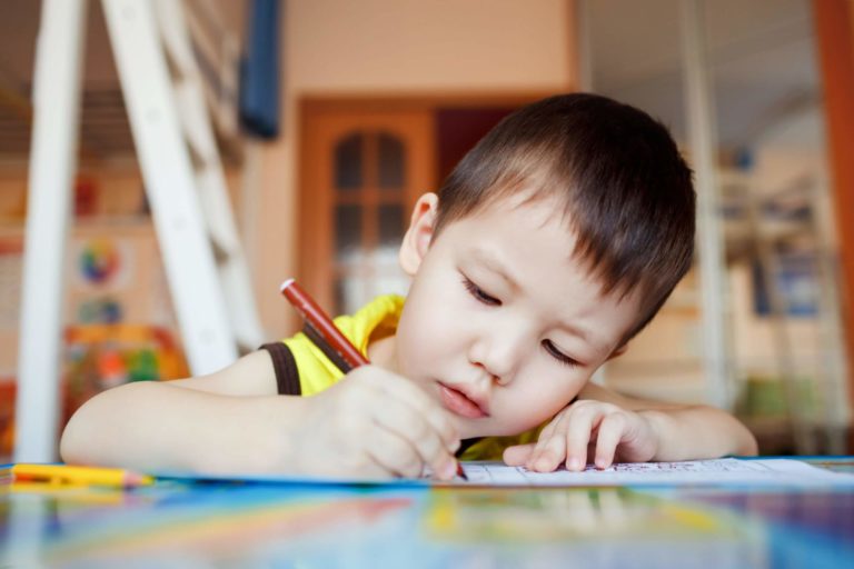 Young boy sitting at a table drawing on paper with a marker.